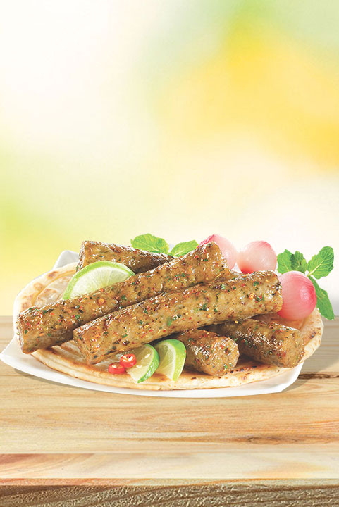A plate with spiced chicken seekh kebabs on a flatbread, garnished with lime wedges, radishes, and mint, served on a wooden surface.