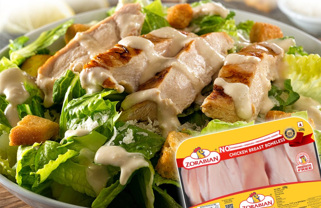 Grilled Zorabian Chicken Breast Boneless slices in a Caesar salad with fresh lettuce, croutons, and creamy dressing, alongside a 450g product pack.