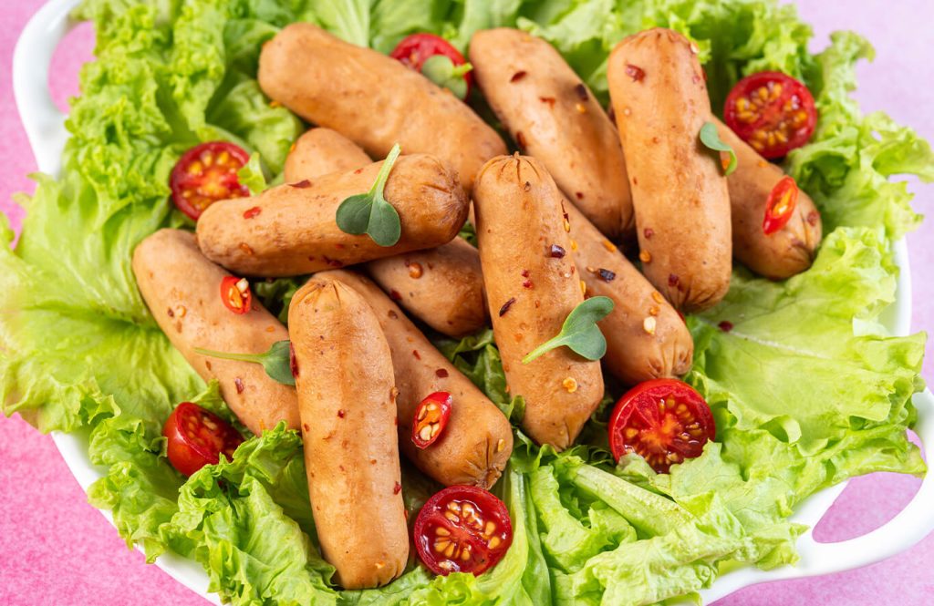 Spicy sausages with lettuce and cherry tomatoes on white plate.