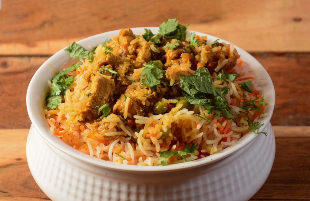 Chicken keema biryani in a white bowl with fresh mint and coriander leaves on a wooden table.