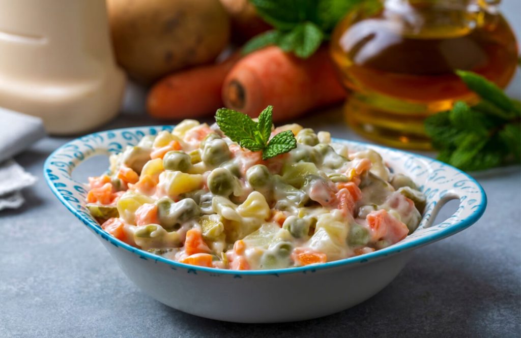 Creamy vegetable salad with potatoes carrots peas in mayonnaise bowl.