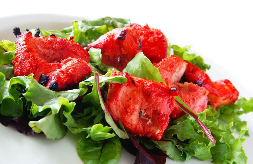Tandoori chicken salad with lettuce on white plate.