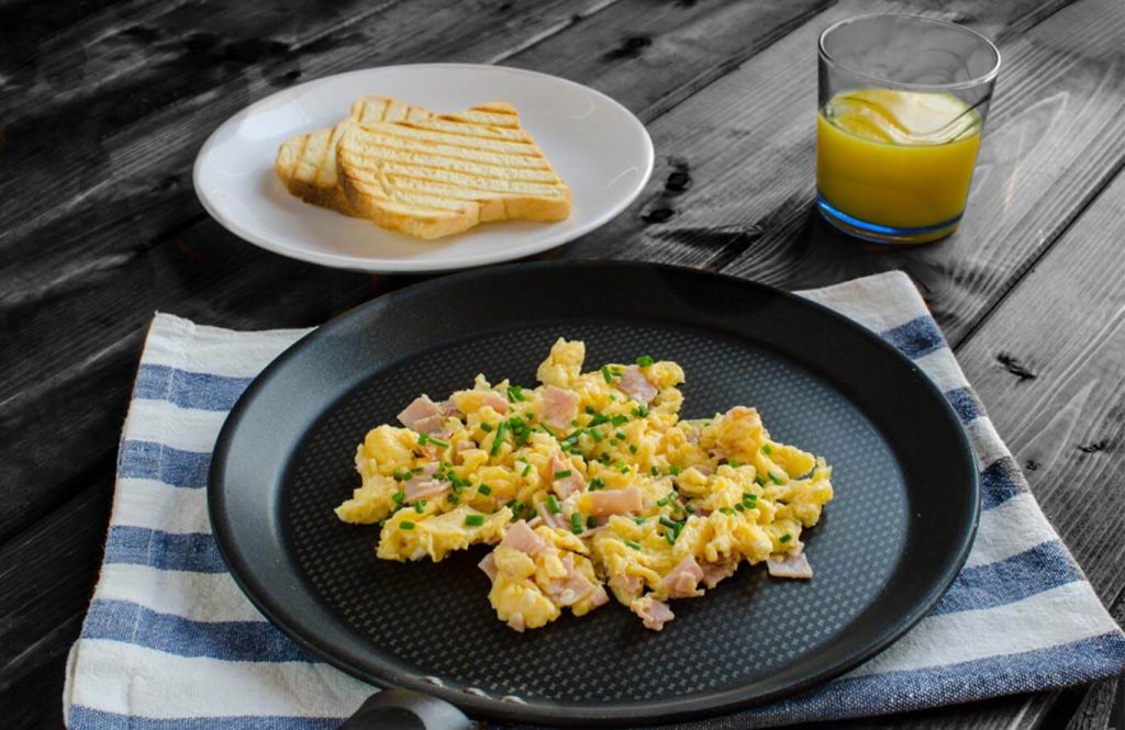 Chicken and egg scramble served on a black plate with toasted bread and a glass of orange juice.