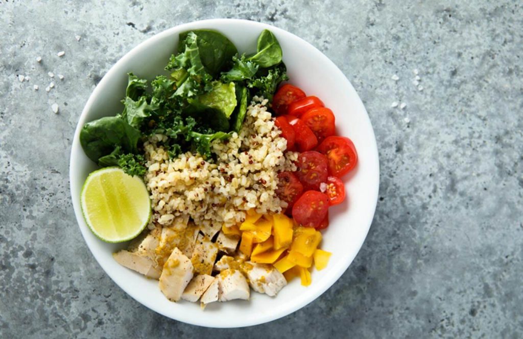 Bowl with cooked quinoa, diced chicken breast, tomatoes, and spinach.