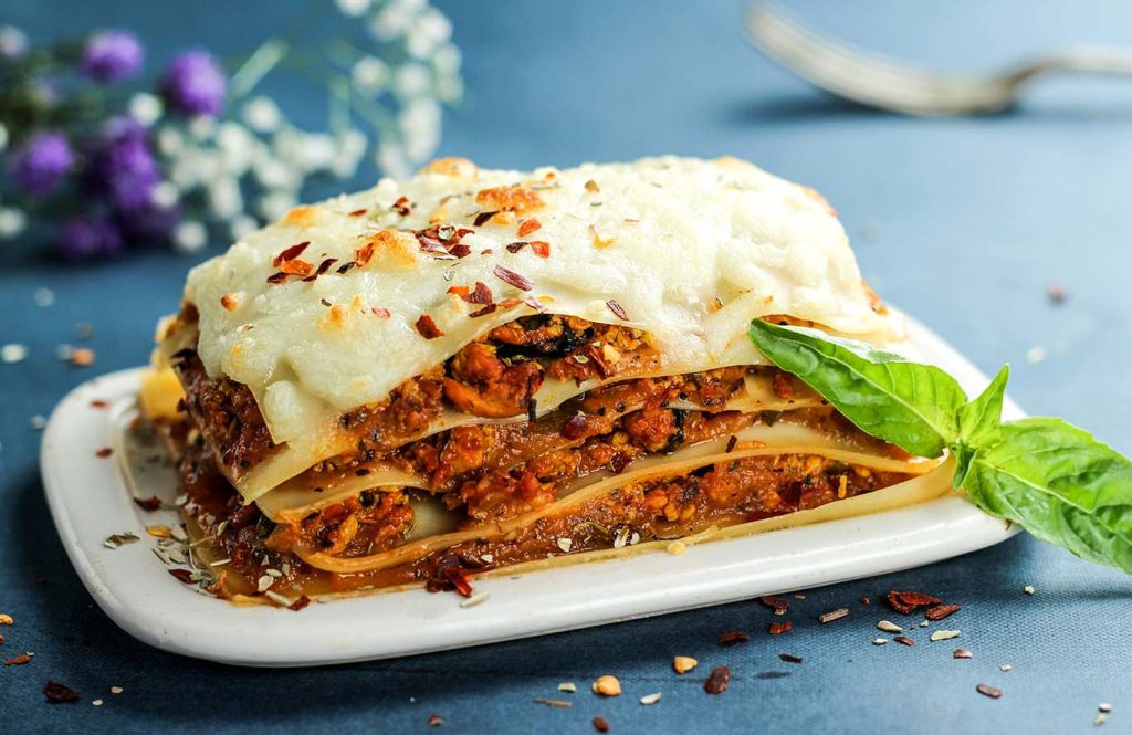 Classic chicken lasagne layered with rich meat sauce, creamy cheese topping, herbs, and fresh basil on a white plate.