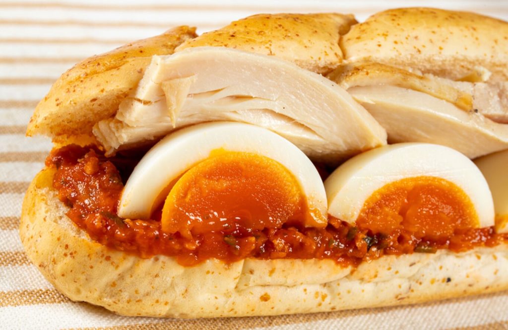 Spicy chicken and egg sandwich with toasted bread, sliced diagonally.