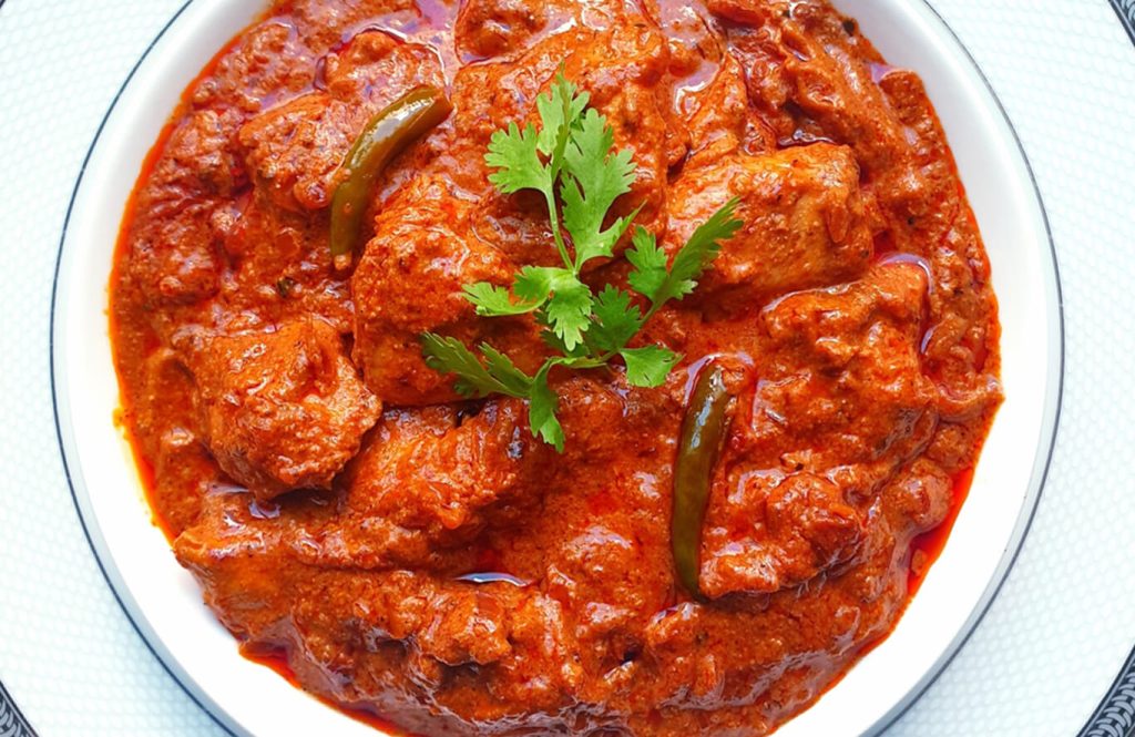 Chicken curry with spiced tomato sauce and rotis, garnished with cilantro.