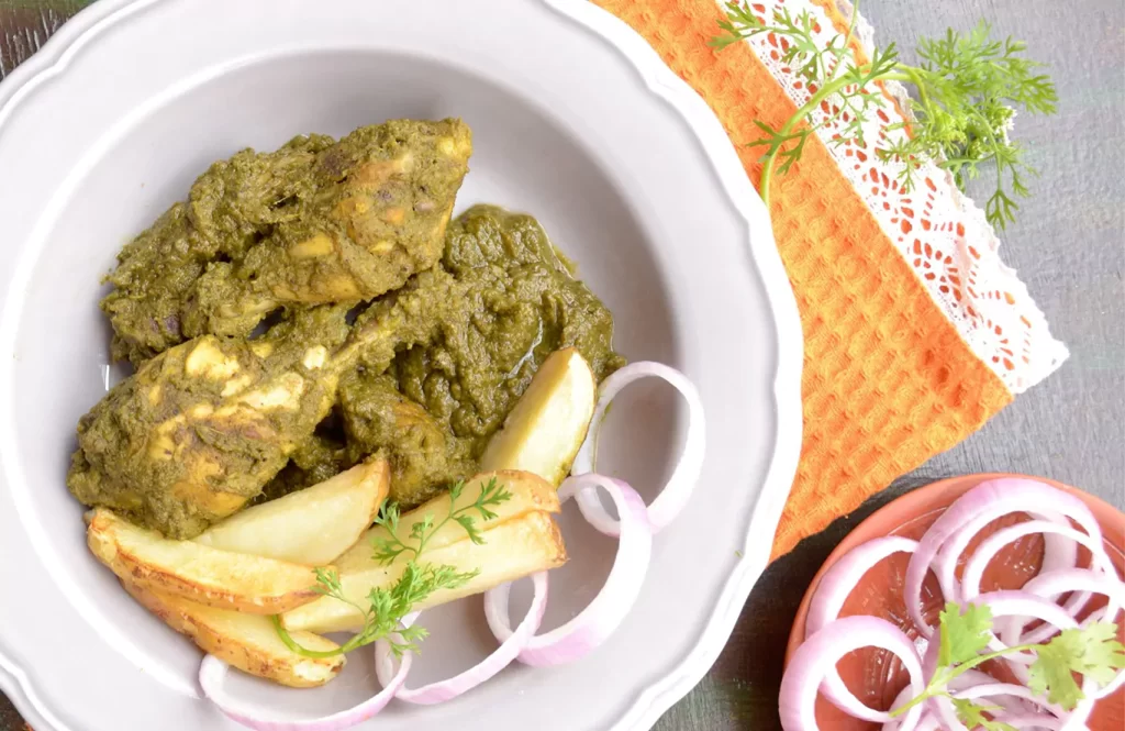 Spicy green Goan chicken curry with coriander marinade, served with boiled potato wedges on a black plate.