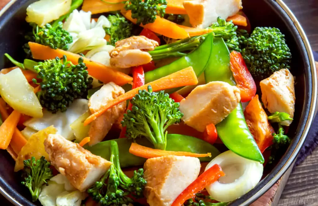 Stir-fried chicken cubes with bell peppers and broccoli in a sesame-soy sauce, served in a meal prep container.