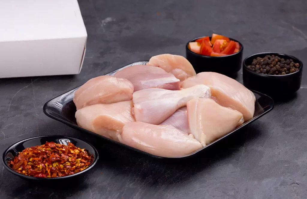 Selection of fresh chicken cuts including boneless breast, legs, mince, and cubes, displayed on a wooden board.