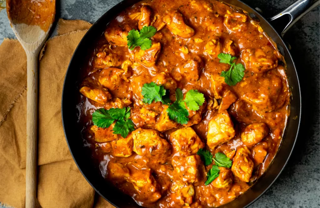 Spicy Goan chicken xacuti curry with coconut and bold spices, garnished with fresh coriander in a pan.