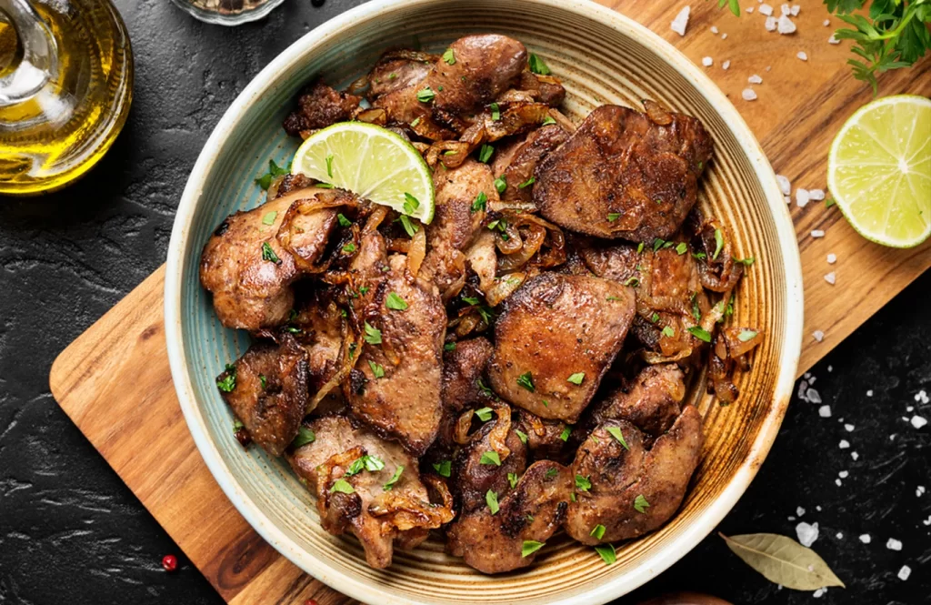 Golden-fried chicken livers coated in spiced flour, served with sautéed onions on a white plate.