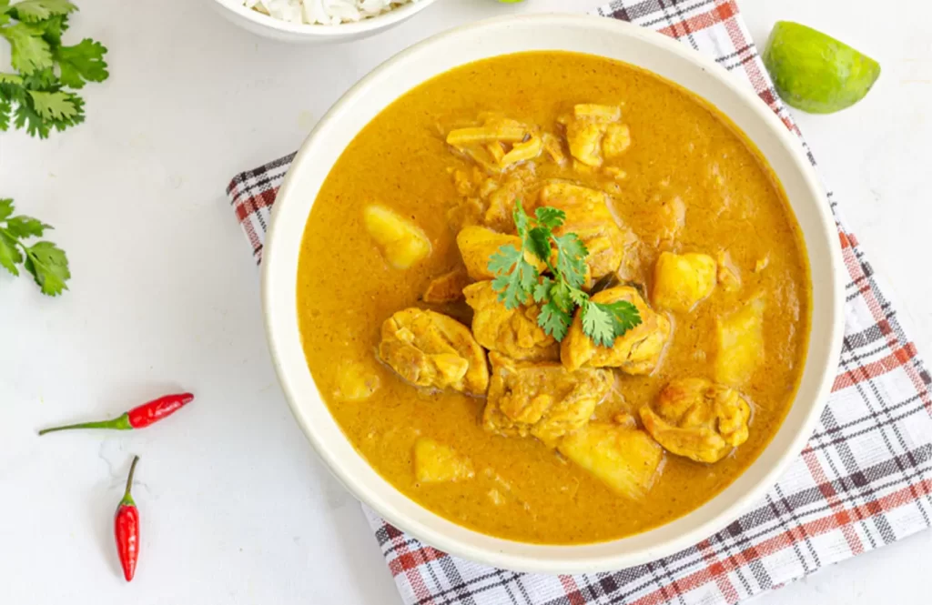 Creamy Goan chicken curry with coconut and tamarind, served with rice on a white plate.