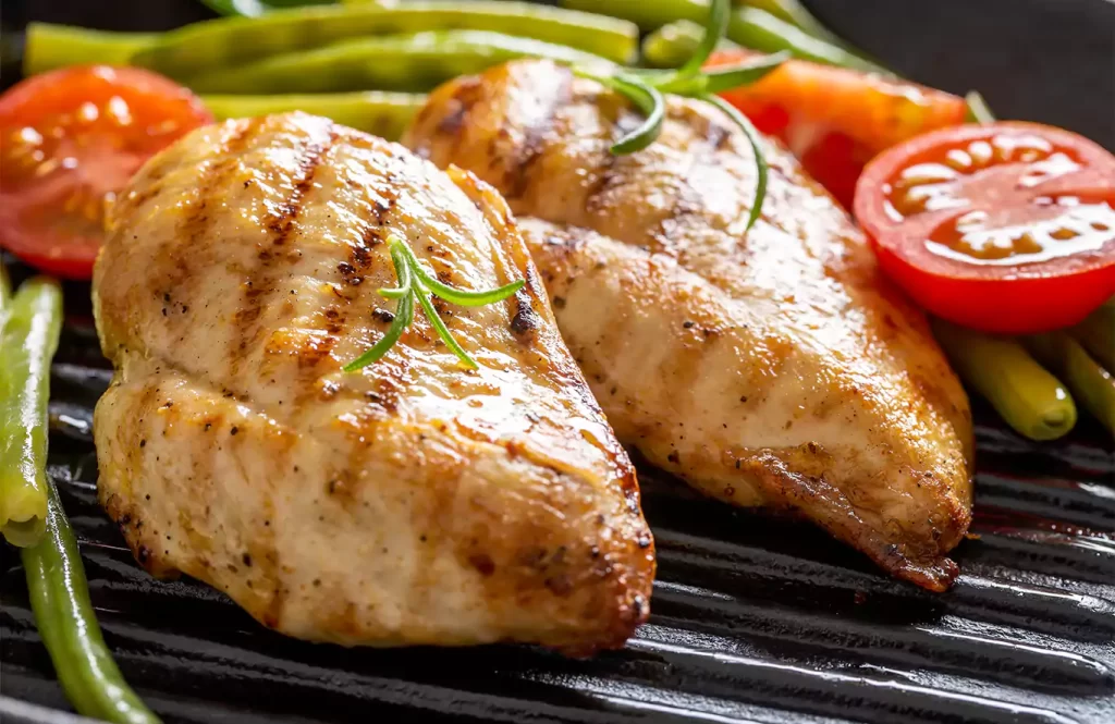 Grilled boneless chicken breasts with lemon zest and oregano, served with steamed green beans on a white plate.