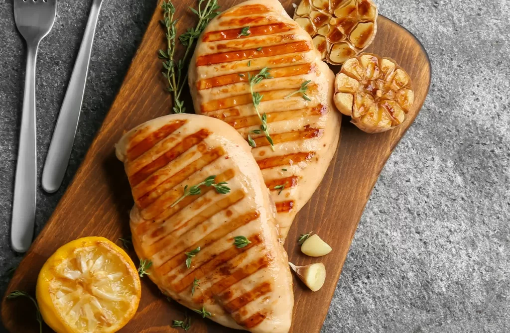 Grilled boneless chicken breast seasoned with paprika and garlic, served on a white plate with lemon wedges on a wooden table.
