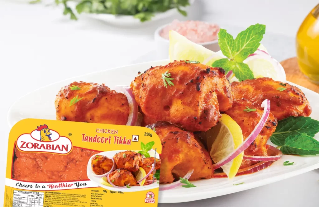 Tandoori chicken tikka pieces with smoky spices, sizzling in a non-stick pan, served with mint chutney on a dark plate.