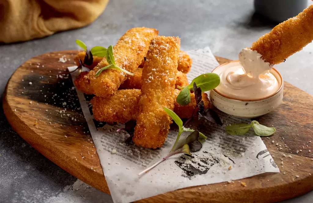 Crispy golden chicken fingers served on a wooden board with creamy dipping sauce.