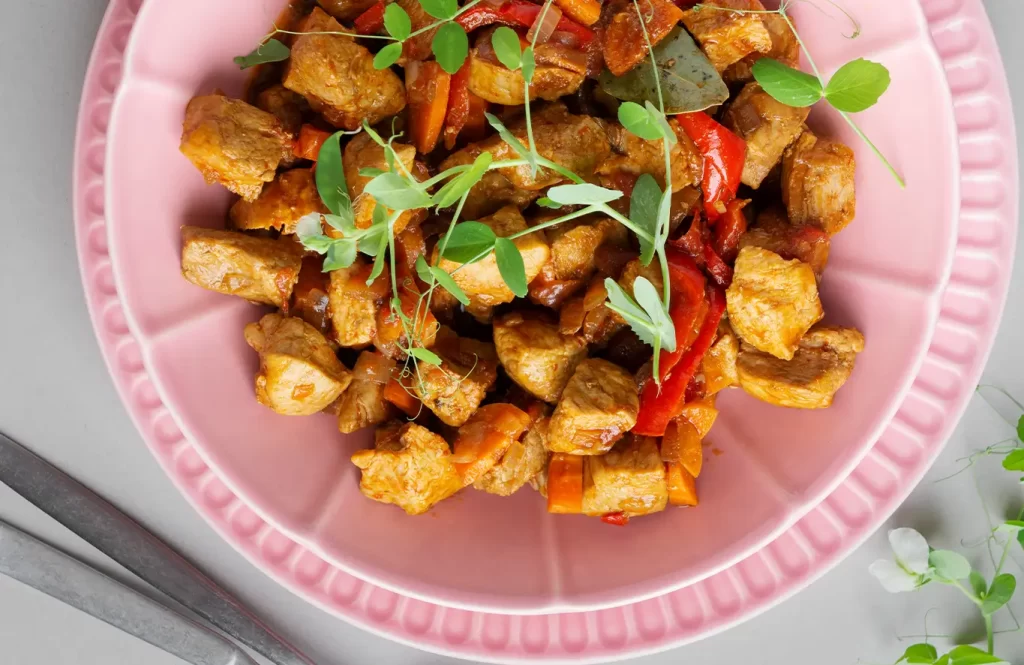 Diced chicken breast with halved cherry tomatoes in a light basil sauce, served in a white bowl.