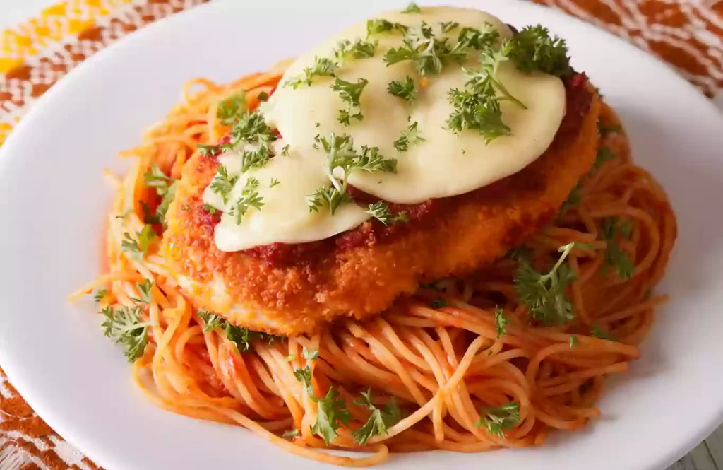 Chicken Parmesan topped with melted cheese and fresh herbs, served over spaghetti in tomato sauce.