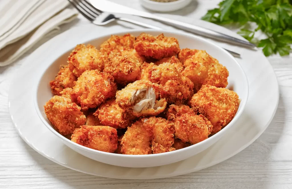 Crispy golden chicken pakora served in a white bowl, made with tender chicken cubes coated in a spiced gram flour batter.