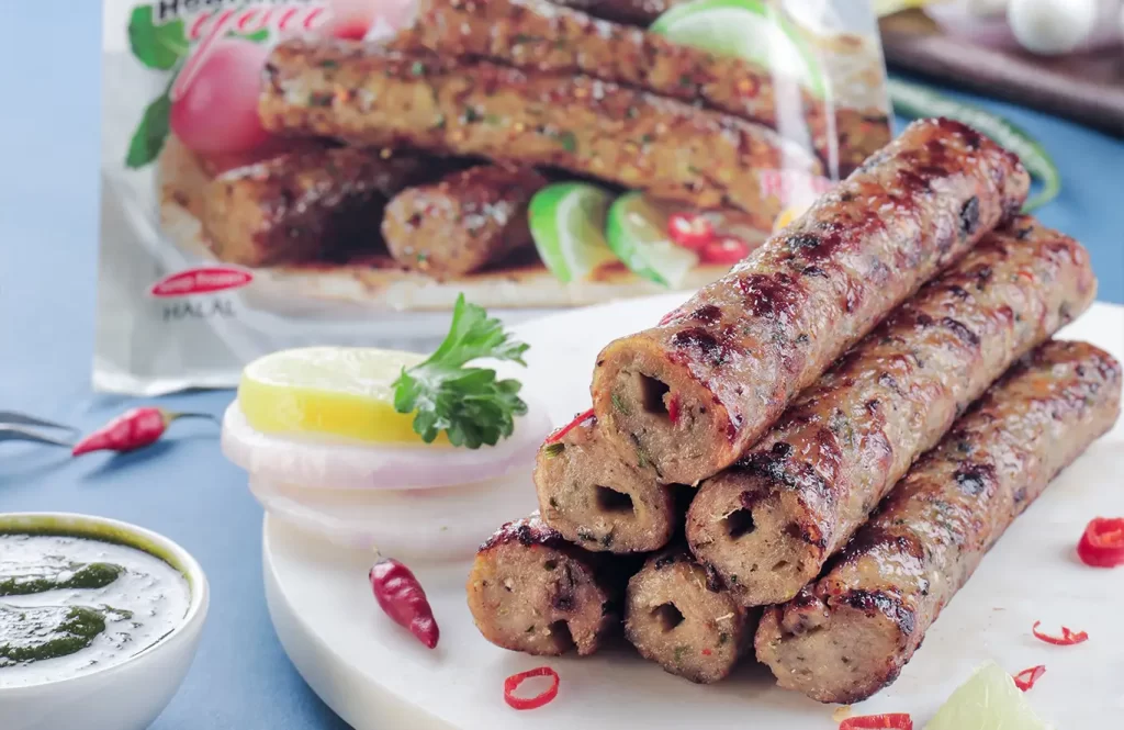 Grilled chicken seekh kebabs served with sliced onions, lemon, and mint chutney on a wooden board.