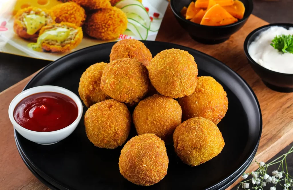Golden crispy chicken cheese balls served with ketchup on a black plate