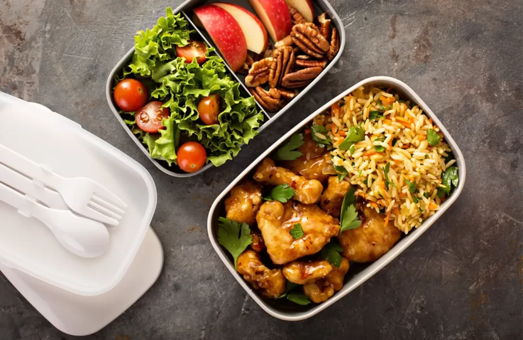 Healthy chicken lunchbox with rice, salad, apples, and pecans.