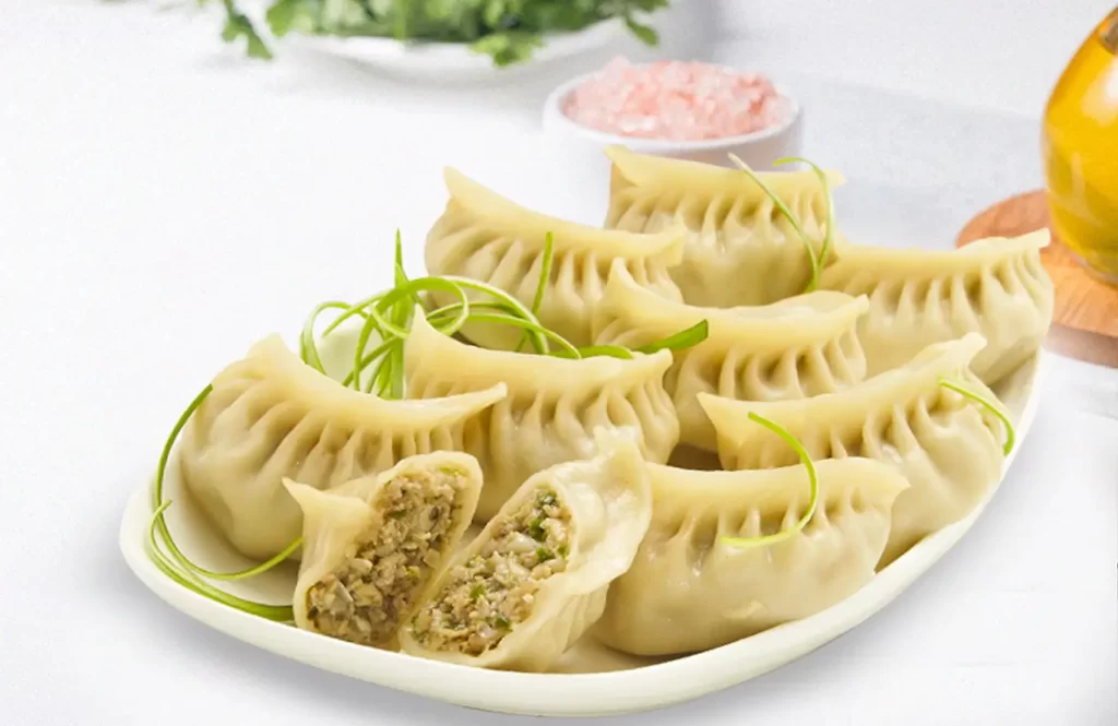 Plate of steamed chicken momos with visible juicy filling and garnished with spring onion curls