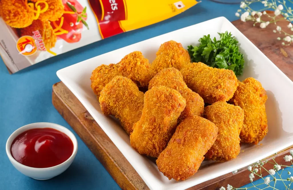 Golden crispy chicken nuggets served in a white plate with ketchup.