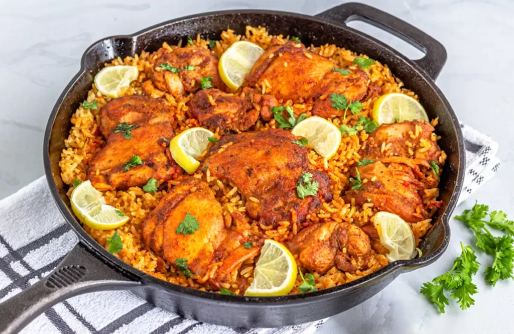 One pot chicken and rice in a cast iron skillet with lemon wedges and fresh coriander garnish