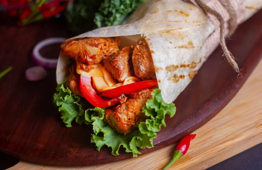 Tandoori chicken wrap with fresh vegetables and lettuce served on a wooden platter.