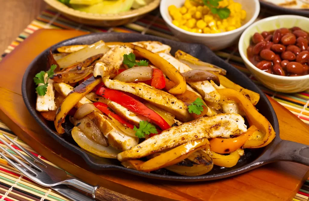 A plate of chicken fajitas with sliced bell peppers, onions, and tender chicken strips, served with warm tortillas and toppings like guacamole and salsa.