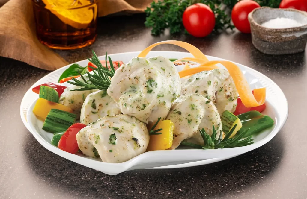 Tender chicken malai tikka bites garnished with fresh herbs and vegetables.