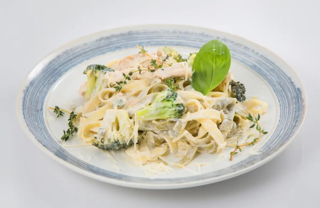 Creamy chicken and broccoli pasta with basil garnish on a white plate.