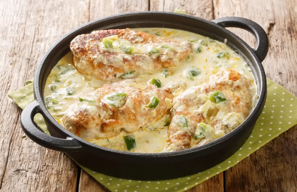 Creamy garlic butter chicken breasts simmered in a rich low carb sauce with fresh green peppers in a black skillet.