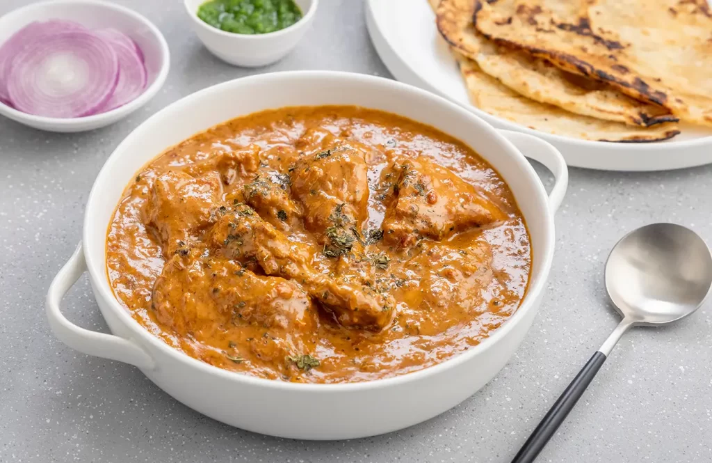 Creamy butter chicken with garlic naan and a tandoori chicken naan wrap with fresh veggies on a rustic table.
