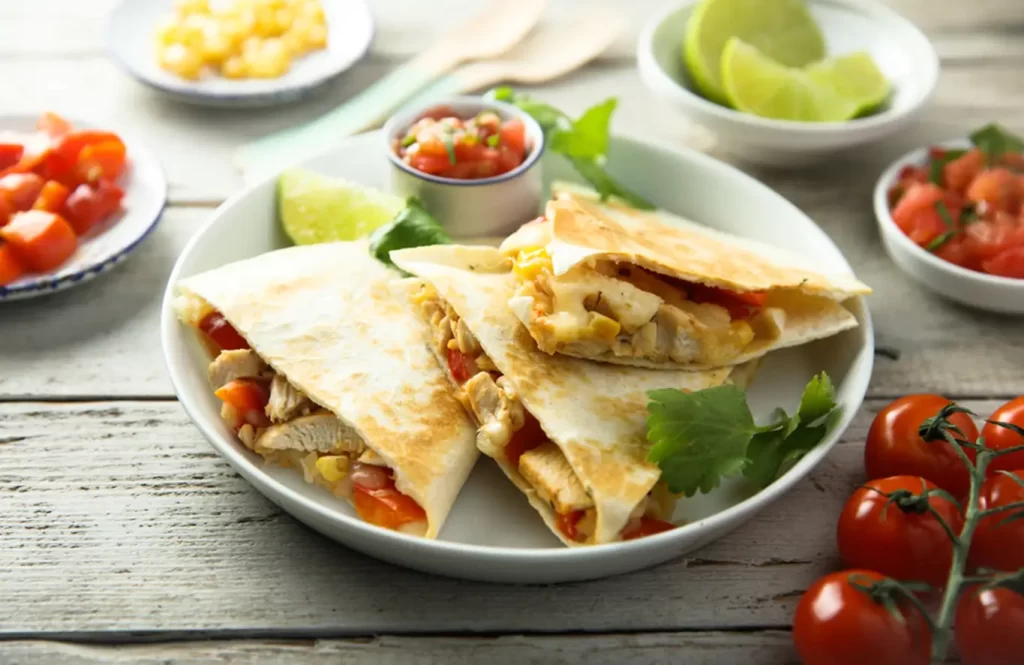 Healthy chicken and veggie quesadillas with salsa and lime on a wooden table.