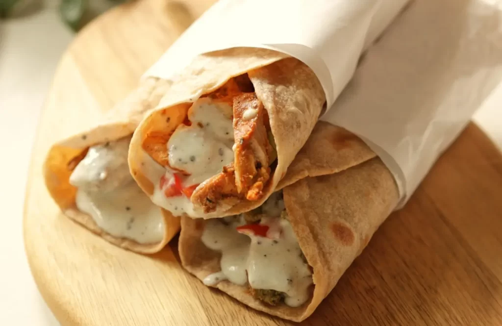 Sliced homemade chicken shawarma with lettuce and tahini sauce in pita bread on a wooden platter.