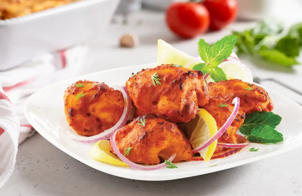 Spiced tandoori chicken tikka skewers served with lemon wedges and onion rings.