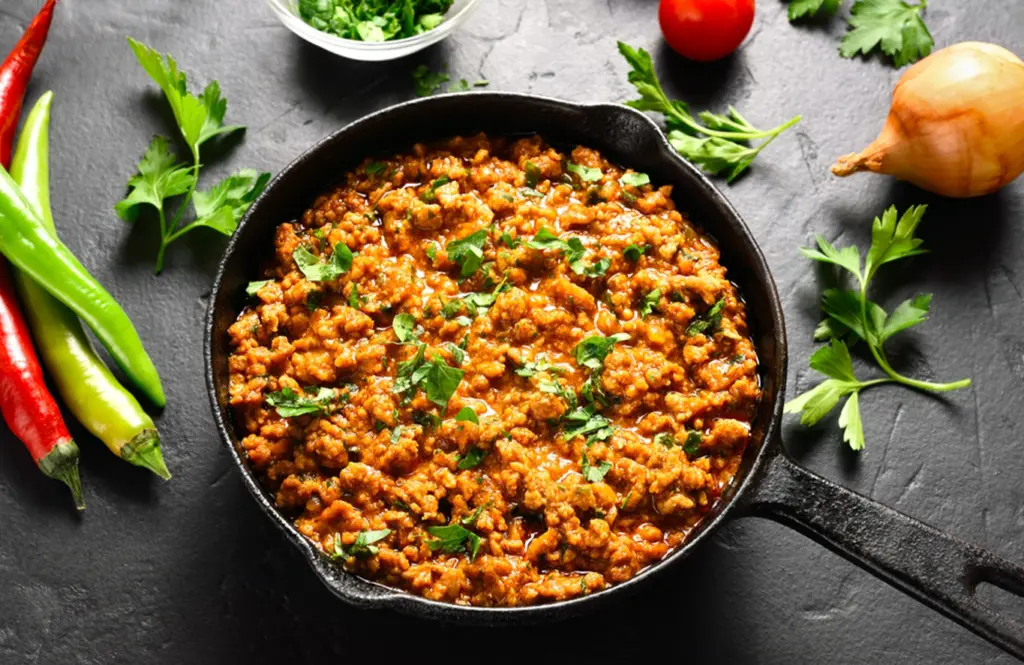 Chicken keema masala in a cast iron pan garnished with fresh coriander on a dark surface.