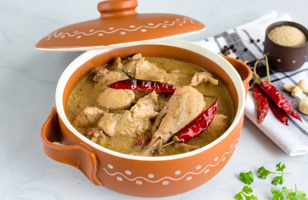 Chicken rezala in a terracotta pot with pale ivory gravy, bone-in chicken and whole red chillies.