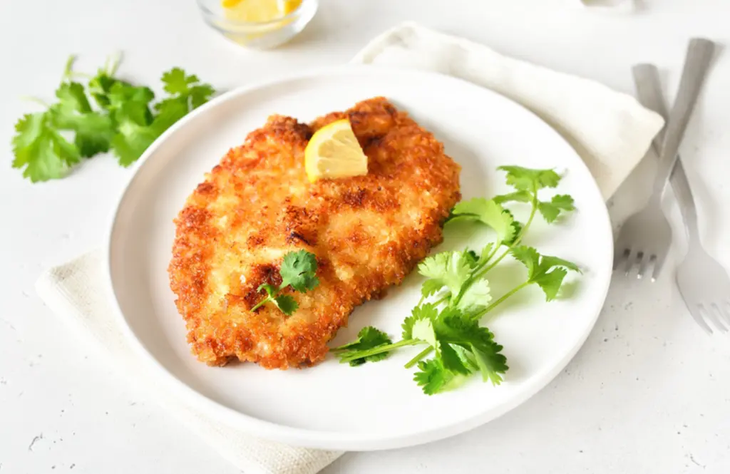 Crispy chicken schnitzel with breadcrumb coating served with lemon wedge on a white plate