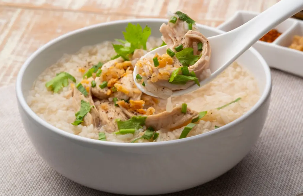 Bowl of chicken congee rice porridge with shredded chicken, scallions and garnish served with a spoon