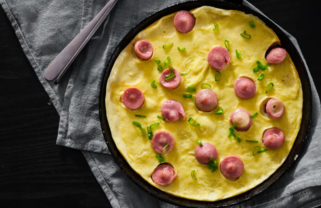 Fluffy omelette with sliced chicken sausages and scallions in a black cast iron skillet