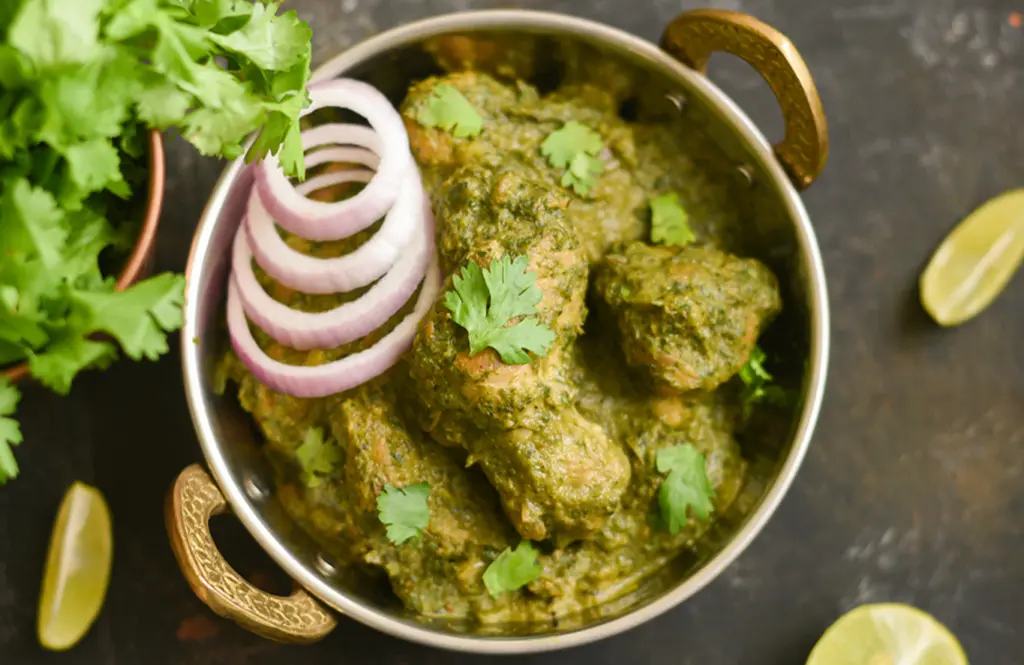 Palak chicken curry with tender chicken pieces in vibrant green spinach gravy served in a brass kadhai