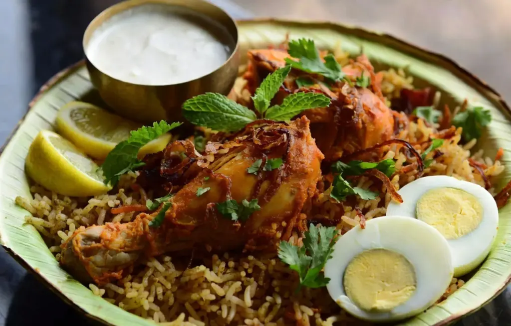 Bengaluru-style Chicken Donne Biryani made with Zorabian Chicken Curry Cut and jeera samba rice served on a banana leaf plate with boiled egg, raita, lemon wedges and fresh mint